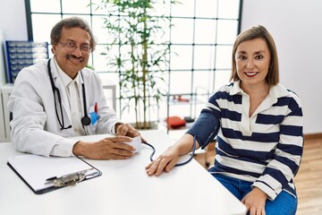 Fototapeta premium Middle age man and woman wearing doctor uniform having medical consultation auscultating using stethoscope at clinic