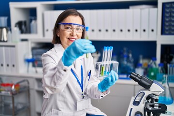Fototapeta premium Middle age woman scientist smiling confident holding test tubes at laboratory