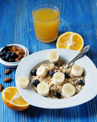 oatmeal with fresh berries, bananas on white plate with orange juice and milk, blue wooden background.