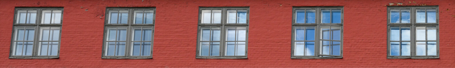 Row of square windows in a red brick wall, blue sky and clouds reflecting in the glass
