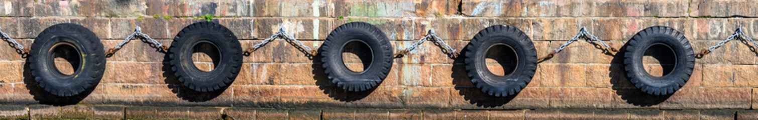 Fototapeta na wymiar Row of old tires chained together against a stone pier as ship bumpers 