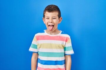 Young caucasian kid standing over blue background sticking tongue out happy with funny expression. emotion concept.