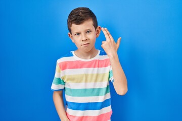 Young caucasian kid standing over blue background shooting and killing oneself pointing hand and...