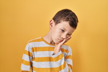 Young caucasian kid standing over yellow background thinking looking tired and bored with depression problems with crossed arms. - obrazy, fototapety, plakaty