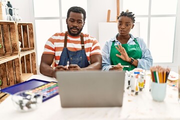 African american painter couple having online paint class sitting on the table at art studio