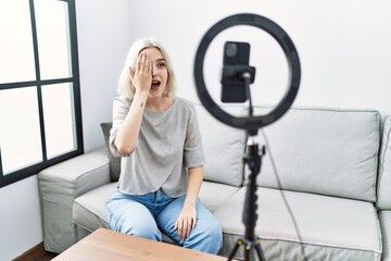 Fototapeta na wymiar Young caucasian woman recording vlog tutorial with smartphone at home covering one eye with hand, confident smile on face and surprise emotion.