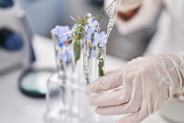 Middle age woman scientist pouring liquid on flowers at laboratory
