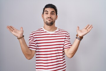 Hispanic man with long hair standing over isolated background clueless and confused expression with...