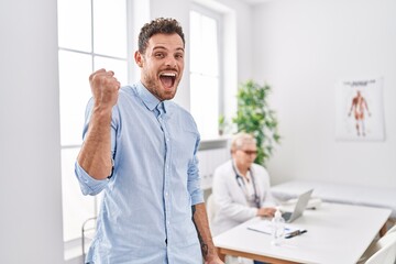 Fototapeta premium Hispanic man at doctor clinic screaming proud, celebrating victory and success very excited with raised arm