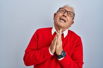 Senior man with grey hair standing over isolated background begging and praying with hands together...