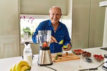 Senior man smiling confident cutting avocado at kitchen