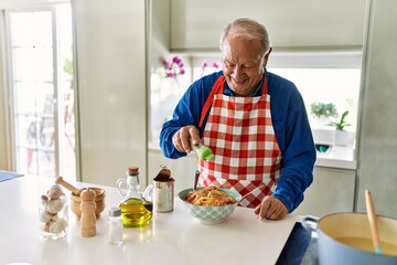 Senior man smiling confident pouring oregano on spaghetti at kitchen