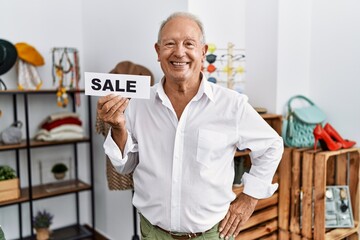 Senior man holding sale banner at retail shop looking positive and happy standing and smiling with a confident smile showing teeth