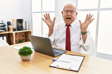 Senior man working at the office using computer laptop celebrating crazy and amazed for success with arms raised and open eyes screaming excited. winner concept