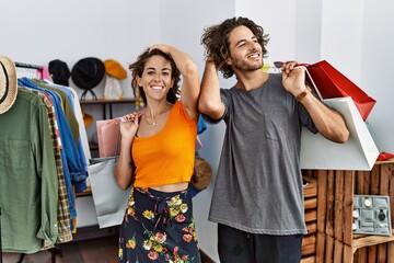Young hispanic couple holding shopping bags at retail shop smiling confident touching hair with hand up gesture, posing attractive and fashionable