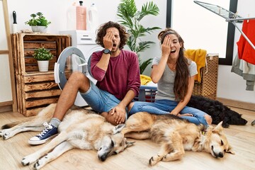 Young hispanic couple doing laundry with dogs yawning tired covering half face, eye and mouth with...