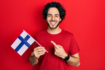 Handsome hispanic man holding finland flag smiling happy pointing with hand and finger