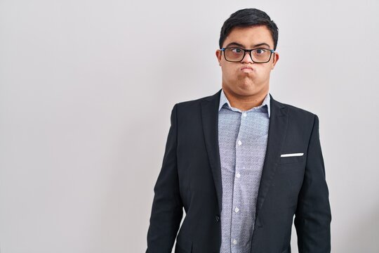 Young hispanic man with down syndrome wearing business style puffing cheeks with funny face. mouth inflated with air, crazy expression.