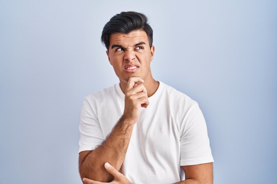 Hispanic man standing over blue background thinking worried about a question, concerned and nervous with hand on chin