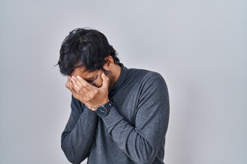 Handsome latin man standing over isolated background with sad expression covering face with hands while crying. depression concept.