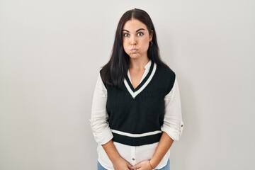 Young hispanic woman standing over isolated background puffing cheeks with funny face. mouth...