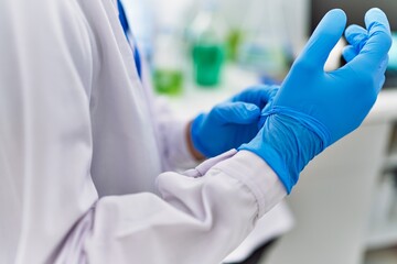Young hispanic man wearing scientist uniform and gloves at laboratory