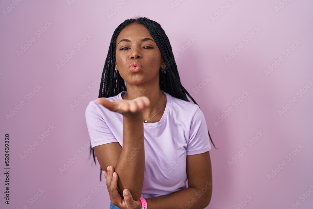 Poster african american woman with braids standing over pink background looking at the camera blowing a kis