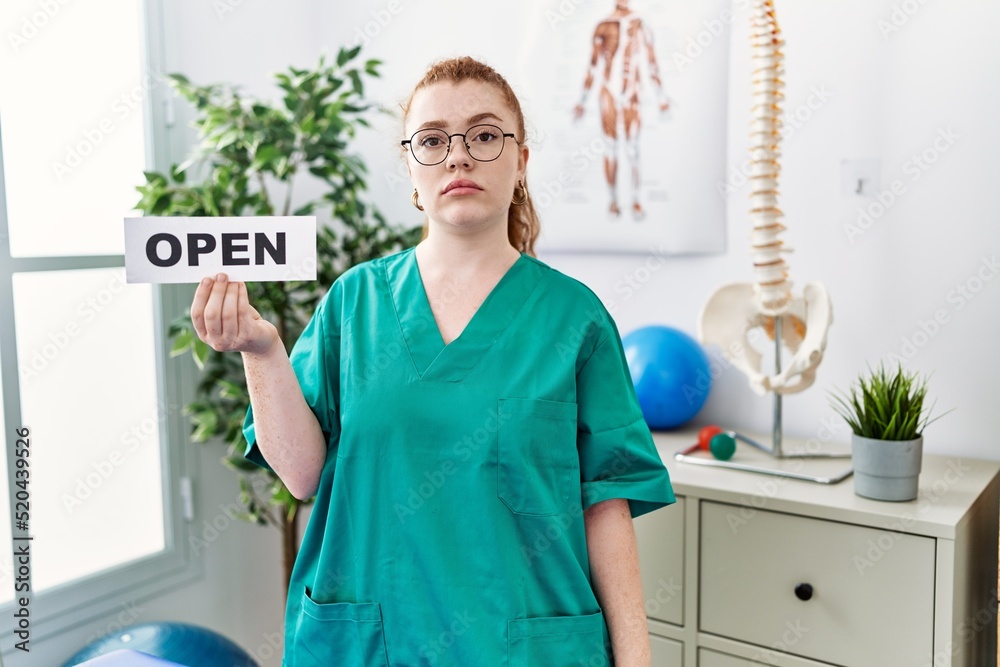 Canvas Prints Young redhead physiotherapist woman working at pain recovery clinic holding open banner thinking attitude and sober expression looking self confident