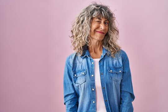 Middle age woman standing over pink background winking looking at the camera with sexy expression, cheerful and happy face.