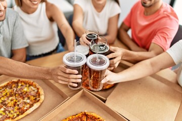 Group of young friends smiling happy eating italian pizza and toasting with cola beverage at home.