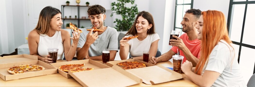 Group Of Young People Smiling Happy Eating Italian Pizza Sitting On The Table At Home