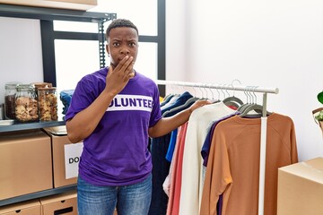 Young african man wearing volunteer t shirt at donations stand covering mouth with hand, shocked and afraid for mistake. surprised expression