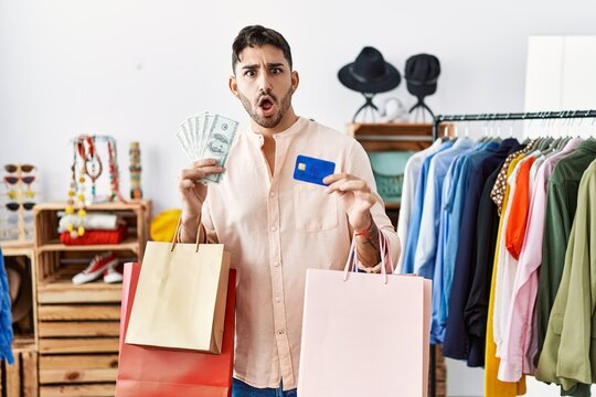 Young hispanic man holding shopping bags and credit card afraid and shocked with surprise and amazed expression, fear and excited face.
