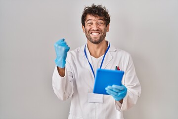 Hispanic scientist man working with tablet screaming proud, celebrating victory and success very excited with raised arms