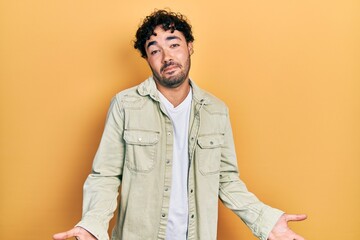 Young hispanic man wearing casual clothes clueless and confused expression with arms and hands...