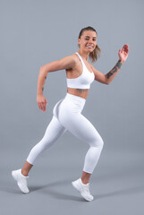 Fototapeta na wymiar Workout sport motivation concept. Young fitness woman runner stretching legs before run. Sporty woman runner on gray background. Dynamic movement. Sport and healthy lifestyle.