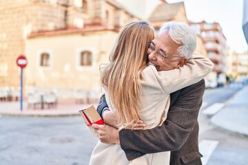 Middle age man and woman couple hugging each other holding gift at street