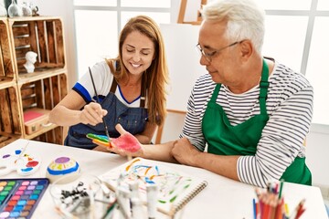 Fototapeta premium Two middle age artists smiling happy painting hands at art studio.