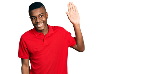 Young african american man wearing casual red t shirt waiving saying hello happy and smiling, friendly welcome gesture