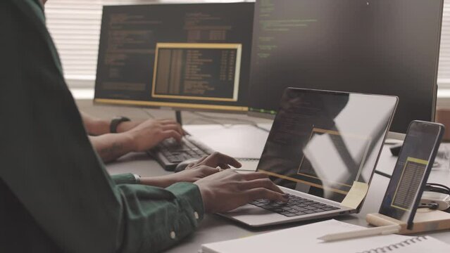 Cropped slowmo of two multiethnic programmers typing program codes on laptop and pc, working together in IT company