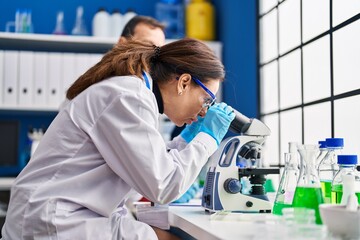 Middle age man and woman scientists using microscope working at laboratory