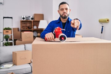 Hispanic man working on moving holding packing tape pointing with finger to the camera and to you, confident gesture looking serious