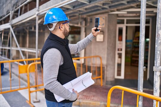 Young latin man architect holding plans make photo by smartphone at street
