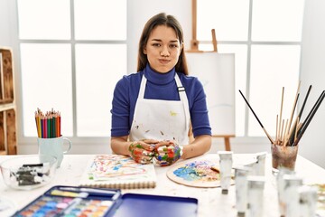 Young brunette woman at art studio with painted hands puffing cheeks with funny face. mouth inflated with air, crazy expression.