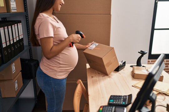Young latin woman pregnant business worker scanning package label at office