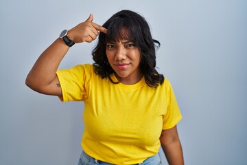 Hispanic woman standing over blue background pointing unhappy to pimple on forehead, ugly infection...