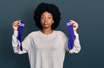 Young african american woman holding socks puffing cheeks with funny face. mouth inflated with air, catching air.