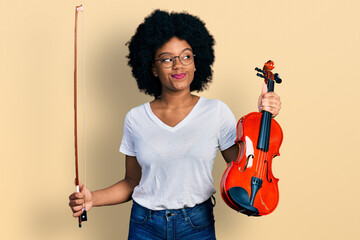Young african american woman playing violin smiling looking to the side and staring away thinking.