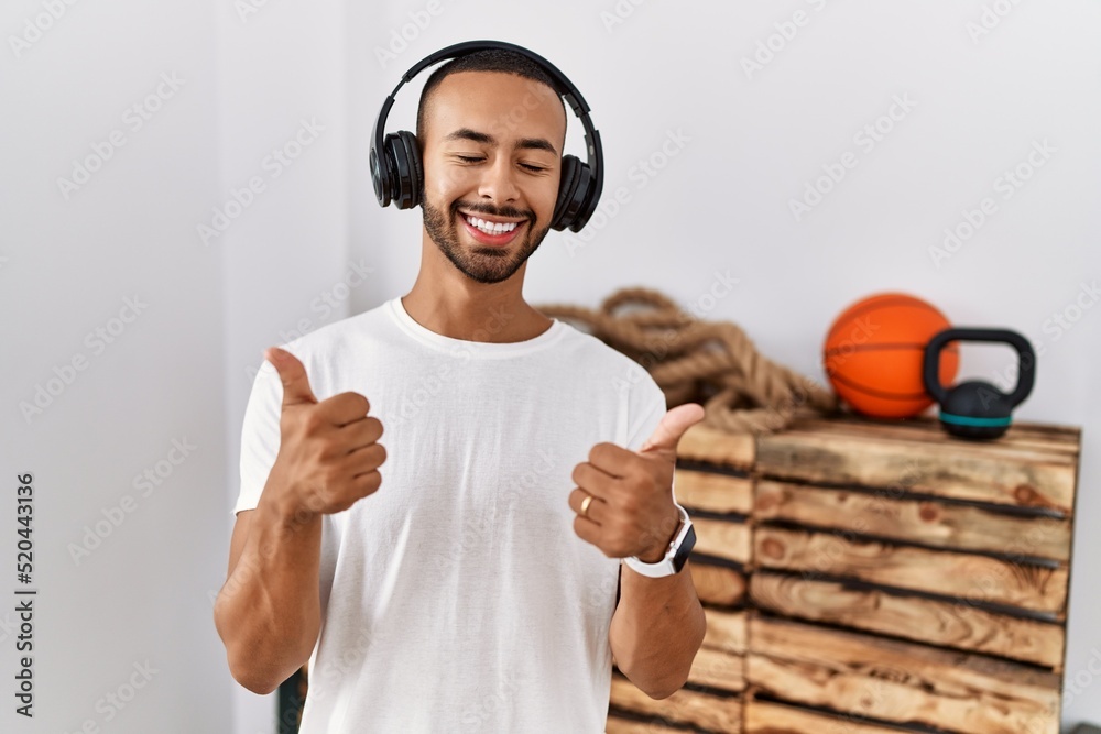 Wall mural african american man listening to music using headphones at the gym success sign doing positive gest