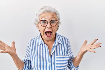 Senior woman with grey hair standing over white background celebrating crazy and amazed for success...